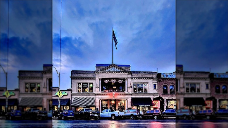 Outside the Palace Restaurant and Salon at dusk with flags flying and vehicles parked in front