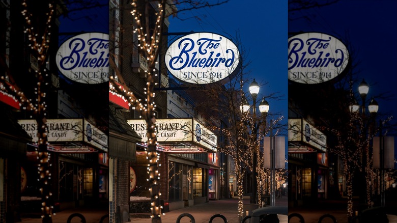 Sidewalk view outside The Bluebird at night with lit signs and trees