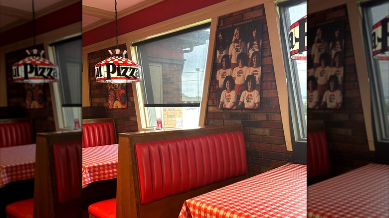 Interior of classic style Pizza Hut restaurant with booth seating, chandeliers, red checkered tablecloths, and trapezoid windows