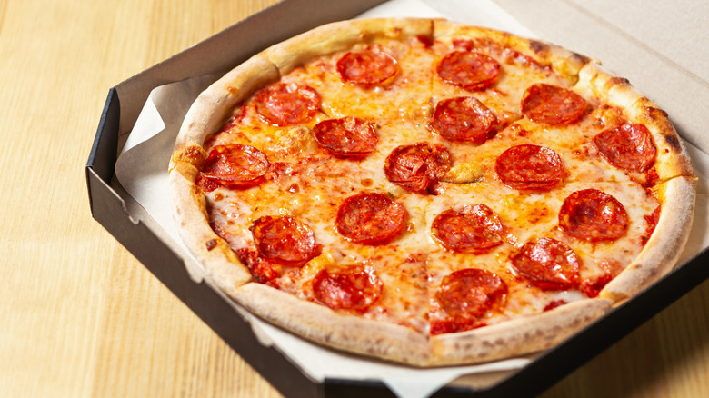 Whole pepperoni pizza inside black cardboard box on wooden surface