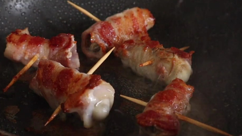Bacon-wrapped oysters grilling in pan