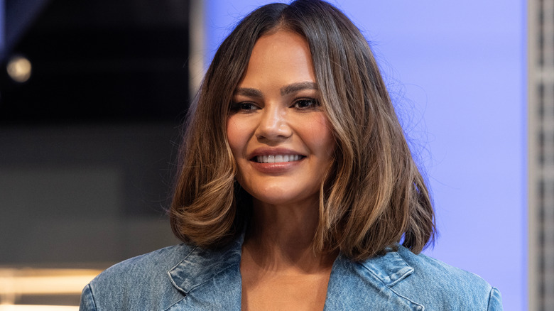 Chrissy Teigen smiles in blue with a long bob hairstyle
