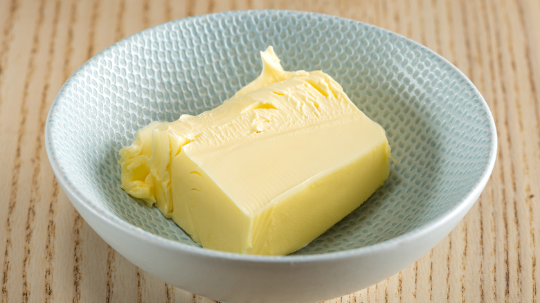 A small bowl with a chunk of butter in it sitting on top of wooden table