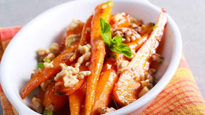 glazed carrots topped with walnuts in a ceramic dish