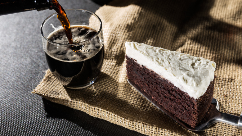 Slice of chocolate cake with white frosting on cake server next to glass of Guinness beer