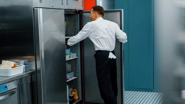 A restaurant employee reaches into a refrigerator