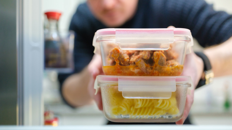 A person places containers of leftovers in the fridge
