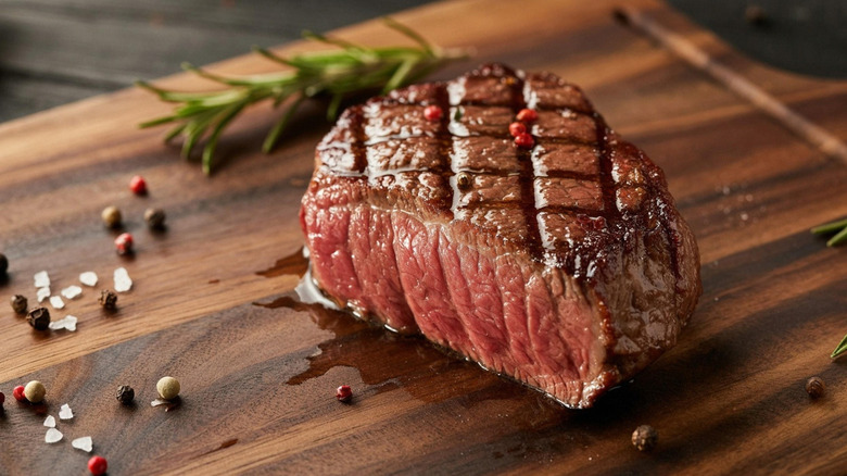 seared steak on a wooden board, salt and pepper granules and herbs behind it