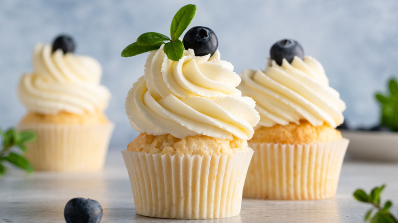 Lovely cupcakes on a raised platter iced with white frosting and topped with a single blueberry