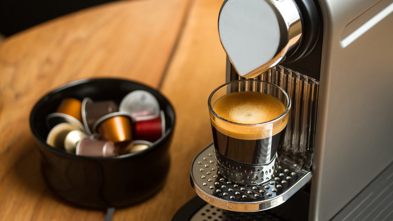 A nespresso machine with a brewed shot and a bowl of pods