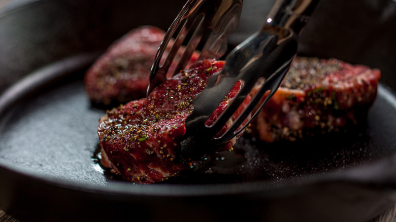 Raw steaks being placed in a pan using tongs