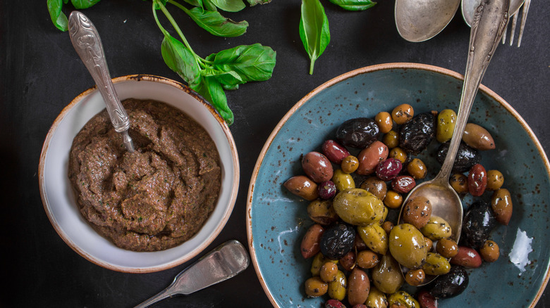 A small bowl of olive tapenade next to a larger bowl of marinated olives