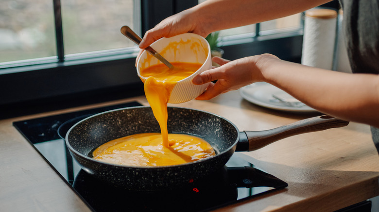 Person pouring omelet mixture into pan