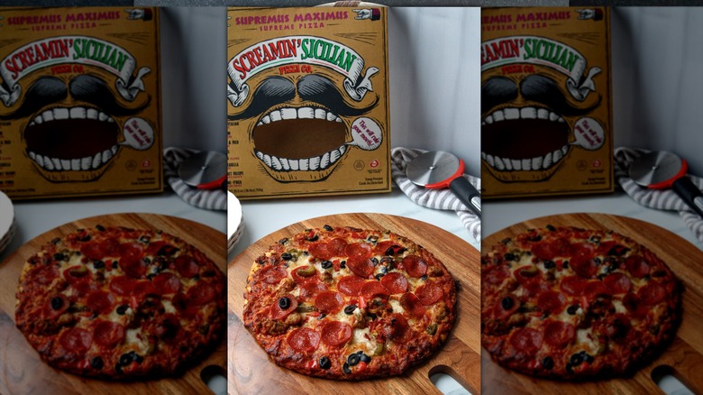 Screamin' Sicilian brand supreme pizza on wooden serving board next to product box