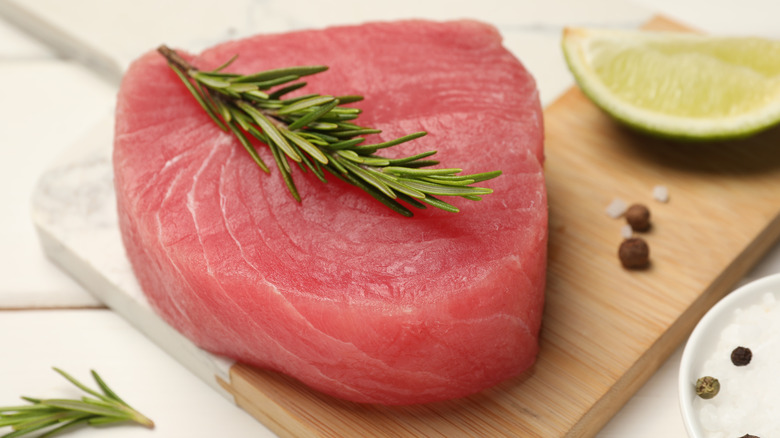Raw ahi tuna steak garnished with rosemary sprig on wooden board