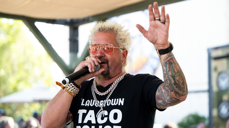 Guy Fieri speaks in microphone with hand in the air