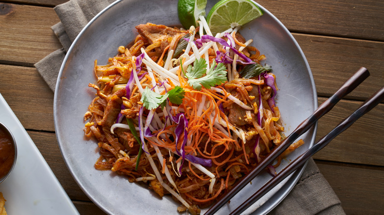 Thai noodle and beef stir fry with lime wedges on gray plate with black chopsticks