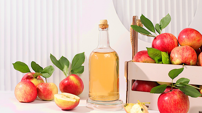 fermented drink in a glass bottle with a cork and lots of apples around.