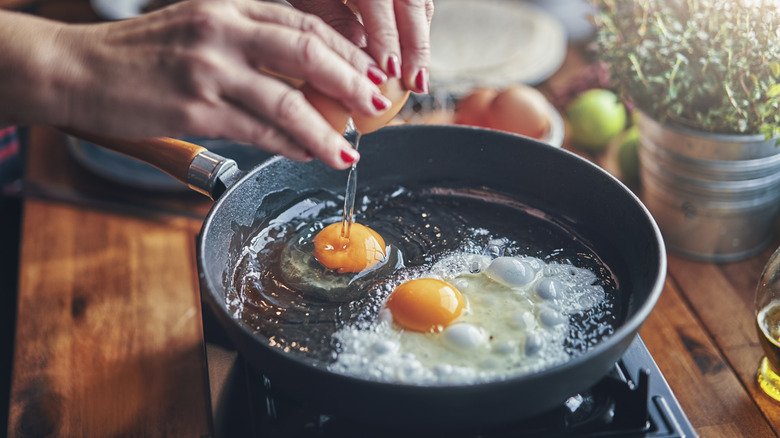 Hands cracking eggs into a pan 