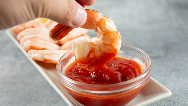 a tail-on shrimp being dipped into a bowl of cocktail sauce