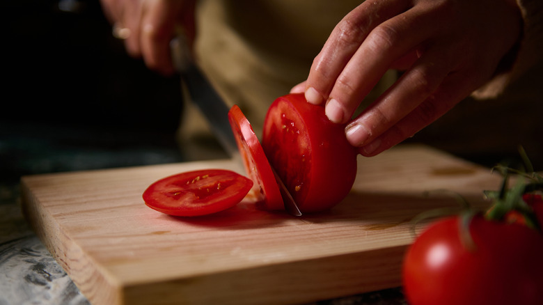 person cutting a slice of tomato
