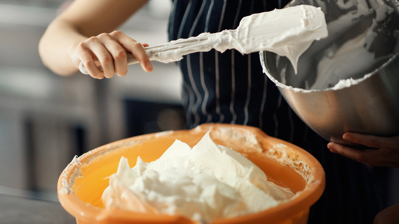 Someone scooping buttercream icing out of one bowl into another