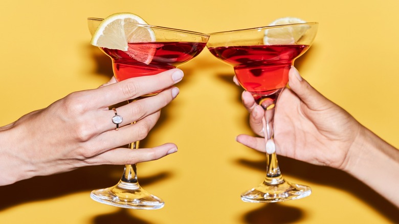 Two hands clinking red cocktails in martini glasses
