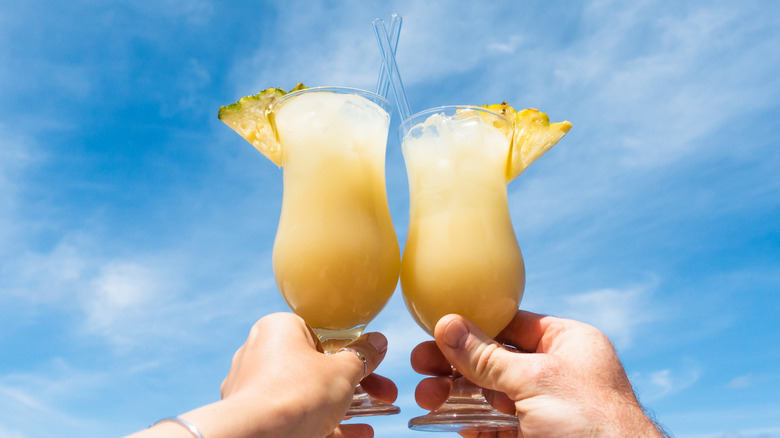 Two people holding piña coladas.