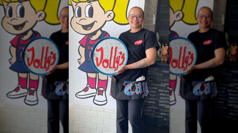 A server in a black uniform holding a Dolly's sparkly tray in front of the Dolly's mascot painting