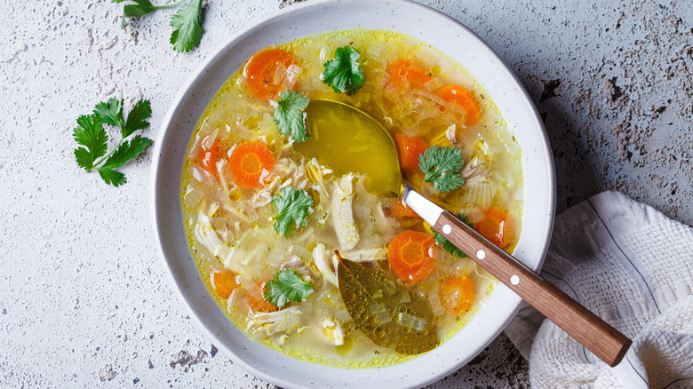 A bowl of chicken noodle soup with spoon inside and cilantro on the side
