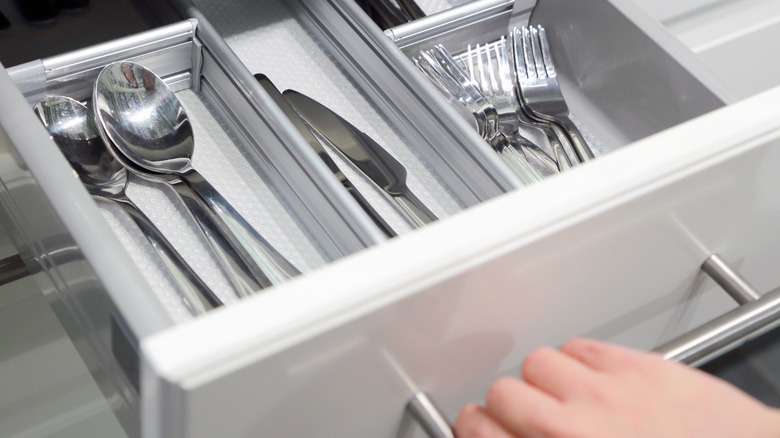 An open silverware drawer showing spoons, butter knives, and forks
