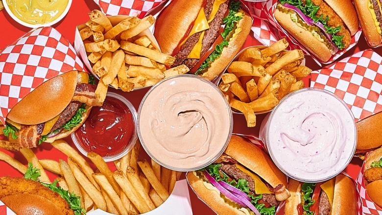 Burgers, fries, milkshakes, and a cup of ketchup on a red tabletop