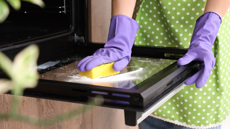 A person cleans an oven door with baking soda