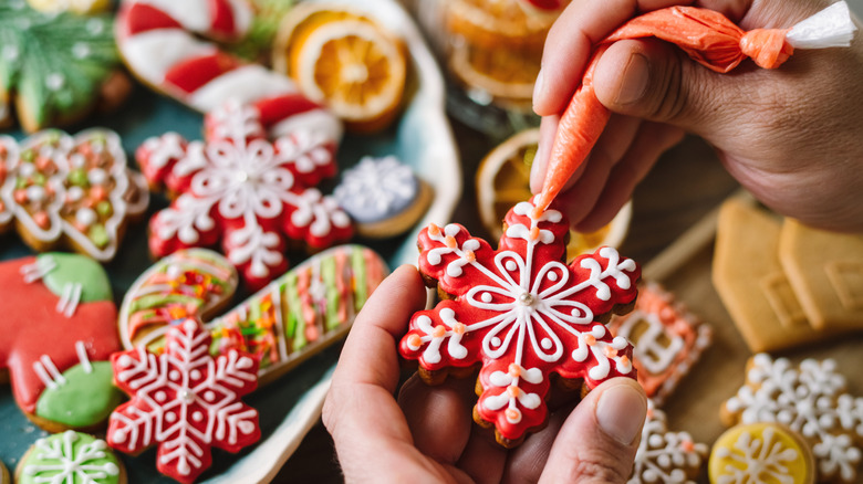 Hands decorating holiday cookies with colored royal icicng.
