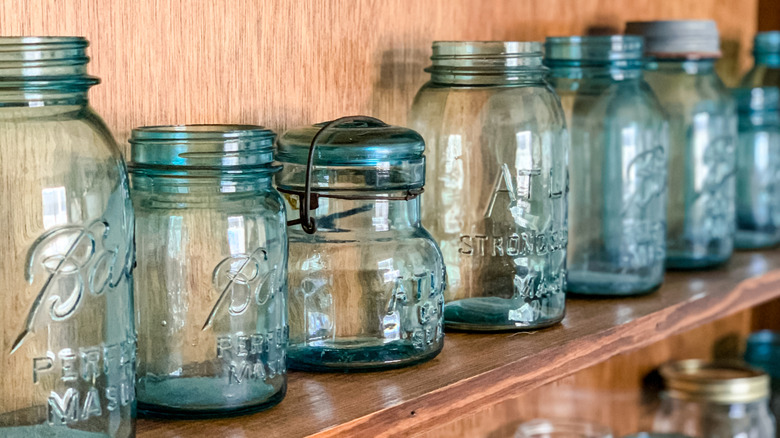 Vintage blue-tinted mason jars from two brands lined up on a wooden shelf.