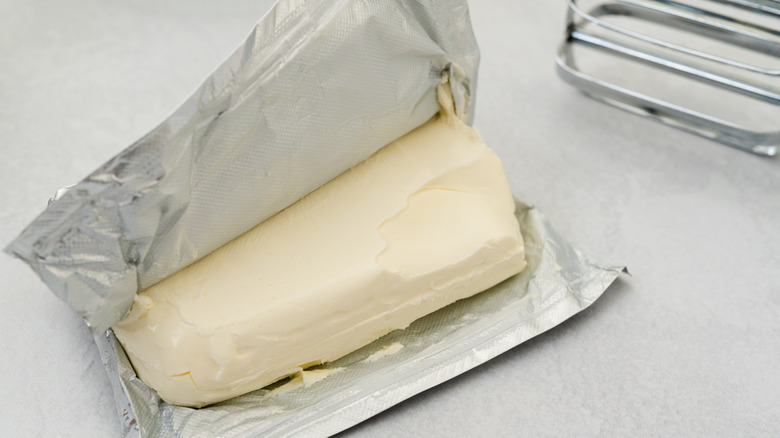 Open packet of cream cheese next to mixer beaters