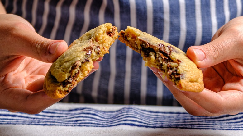 a person holds two halves of a chocolate chip cookie