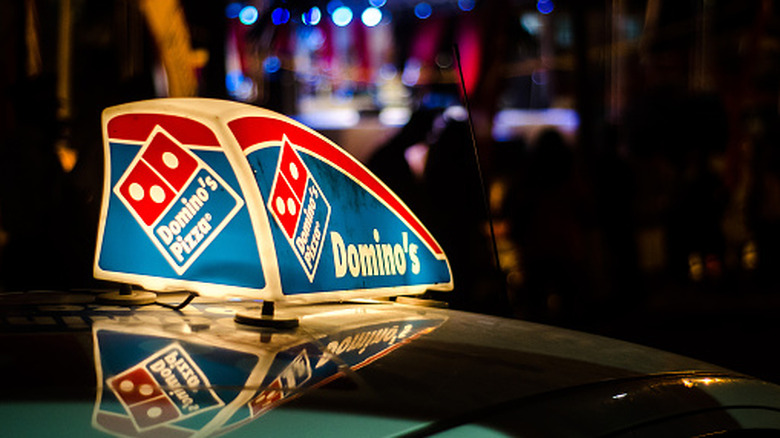 A Domino's light-up sign on top of a delivery car.