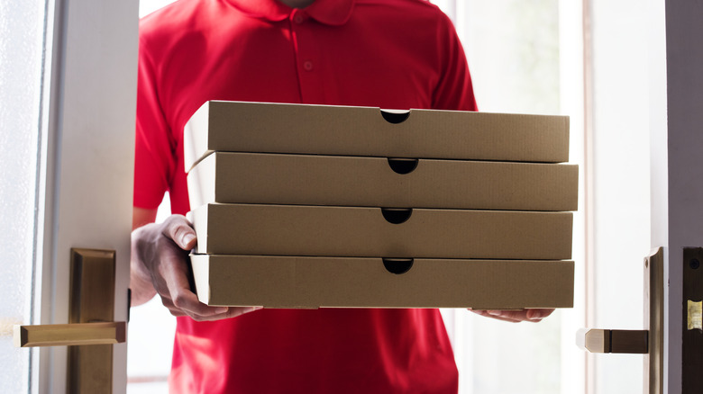 A delivery person in a red polo delivering pizza boxes.