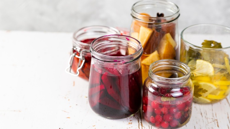 Five jars of drinking vinegar infusions made with cranberries, lemon and other fruits