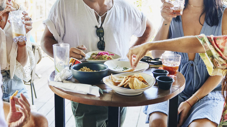 A group of people sit around a table at a restaurant with appetizers and drinks.