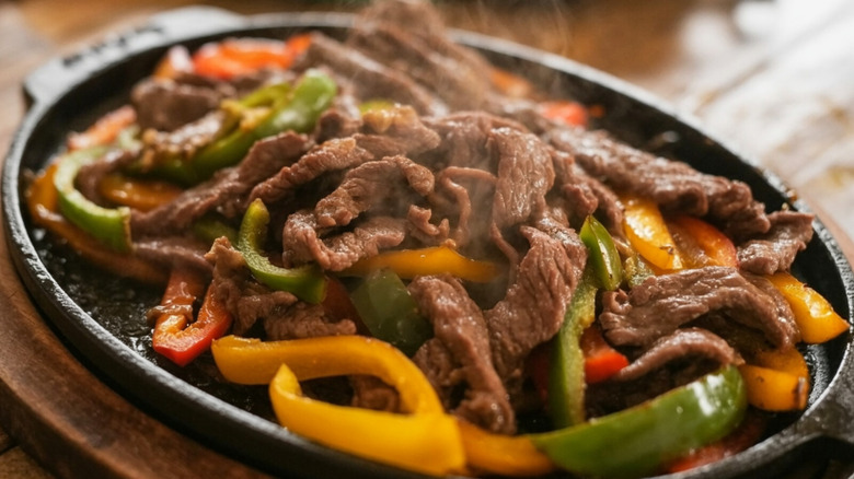 A plate of beef enchiladas and peppers in a black skillet