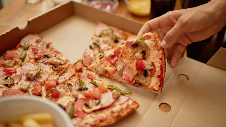 A hand grabbing a slice of pizza out of a carboard box
