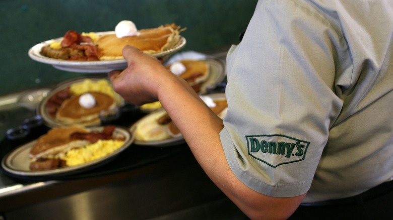 Denny's server carrying a plate of food with other meals in background