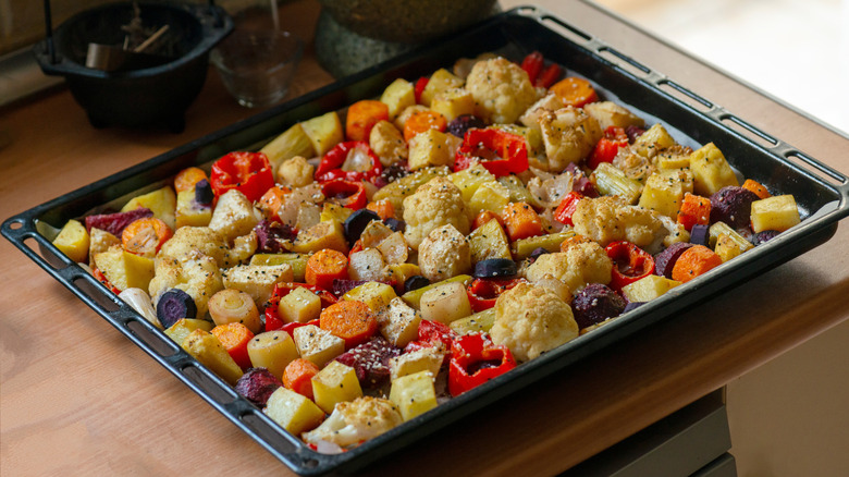 Tray of oven roasted vegetables including potatoes, carrots, and peppers