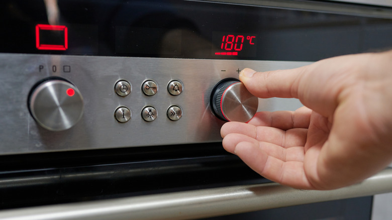 Person turning oven temperature up, with 180 degrees C appearing on the display