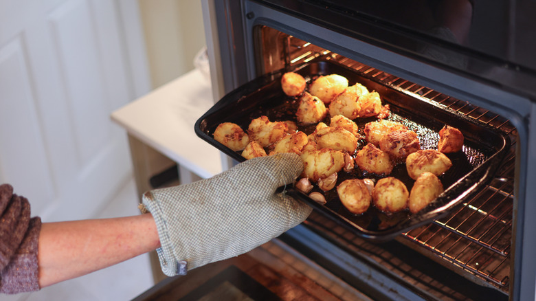 Person baking a tray of roasted potatoes in the oven