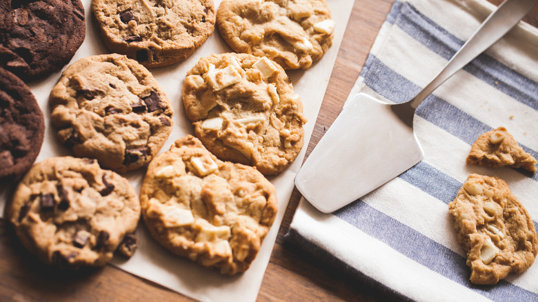 A tray with chocolate, chocolate chip, and white macadamia nut cookies beside a serving spoon