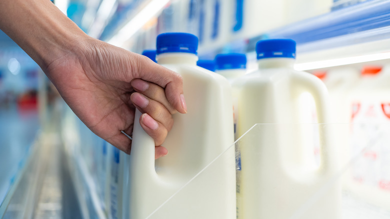 Hand grabbing milk from grocery store shelf