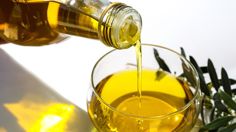 Bottle pouring olive oil into small glass bowl